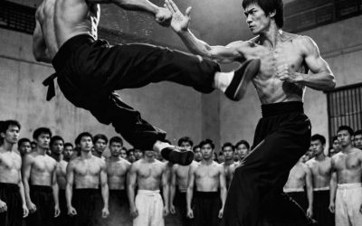 În vara anului 1967, cel mai prestigios dojo din Los Angeles urma să fie scena unei confruntări care avea să rămână întipărită în memoria tuturor celor prezenți. Joe Lewis, campion național la karate cu un palmares perfect de 32 de victorii consecutive, tocmai făcuse o declarație care avea să zguduie lumea artelor marțiale: susținea că este mai rapid decât Bruce Lee. Aroganța sa nu era nefondată. Cu o înălțime de 1,98 m și o greutate de 95 kg de mușchi puri, își zdrobise toți adversarii. Pumnii săi loviseră ca fulgerul, iar loviturile lui puseseră la pământ peste o duzină de luptători. Dar ceea ce avea să se întâmple în acea după-amiază avea să-i schimbe nu doar viziunea asupra artelor marțiale, ci întreaga sa viață. Totul începuse cu trei săptămâni mai devreme, în timpul unui interviu pentru o revistă de specialitate. Jurnalistul îl întrebase pe Lewis ce părere are despre Bruce Lee, instructorul chinez care începea să-și facă un nume la Hollywood cu demonstrațiile sale revoluționare. Lewis, cu un zâmbet batjocoritor pe buze, a răspuns direct: „Bruce Lee?” „E doar un showman”, a declarat el, lăsându-se în scaun cu brațele încrucișate. „Face acrobații pentru camere, dar într-o luptă adevărată, viteza și forța mea l-ar doborî în mai puțin de treizeci de secunde. I-am înfruntat pe cei mai buni din țară și niciunul dintre ei nu a rezistat mai mult de două minute împotriva mea.” Cuvintele lui s-au răspândit ca focul în paie prin comunitatea artelor marțiale. La acea vreme, Bruce Lee nu era încă legenda filmului pe care lumea avea să o cunoască mai târziu. Era pur și simplu un instructor cu idei revoluționare despre luptă, dezvoltându-și propriul sistem: Jeet Kune Do. Când afirmațiile lui Lewis au ajuns la Bruce Lee, acesta nu s-a înfuriat. A zâmbit pur și simplu, cu calmul care i-a derutat pe cei care îl cunoșteau. Ținea o lecție privată în micul său dojo din Chinatown când un elev i-a arătat articolul din revistă. „Maestre, ai de gând să răspunzi la asta?”, a întrebat elevul, așteptându-se la o furie. Bruce a împăturit cu grijă revista și a așezat-o pe masă. Ochii lui întunecați străluceau cu un amestec de amuzament și hotărâre. „Nu trebuie să răspund în cuvinte”, a spus el simplu. „Cuvintele sunt doar vânt.” „Adevărul se arată în acțiune.” În aceeași după-amiază, Bruce a făcut ceva neașteptat: a sunat la dojo-ul unde se antrena Joe Lewis. Conversația a fost scurtă, dar semnificativă. Bruce nu încerca să-l provoace sau să-l insulte. Dimpotrivă, i-a adresat o invitație care l-a lăsat perplex pe campion. „Am auzit că ești cel mai bun”, a spus Bruce politicos, dar ferm. „Aș vrea să vii la dojo-ul meu sâmbătă după-amiază, nu să luptăm, ci să ne antrenăm împreună. Cred că am putea învăța unul de la celălalt.” „Ce crezi?” Luat prin surprindere,Lewis a simțit cum i se umflă egoul. A interpretat invitația ca pe o recunoaștere a inferiorității și a acceptat imediat, nerăbdător să demonstreze că Bruce Lee nu era decât aer cald. Sâmbăta a adus căldura tipică Californiei. Micul dojo al lui Bruce Lee, din Chinatown, la etajul doi al unei clădiri vechi, avea podea de lemn, saci de box și echipament minimal – fără oglinzi luxoase sau aparate sofisticate. Joe Lewis a sosit cu trei studenți loiali, emanând încredere și siguranță de sine. Gi-ul său alb imaculat și centura neagră perfect înnodată, împreună cu fiecare gest autoritar al său, îl făceau să pară imaginea unui campion neînvins. Bruce Lee îl aștepta în centrul dojo-ului, îmbrăcat simplu, în pantaloni negri și desculț… …Va urma în comentarii.👇Vezi mai puțin